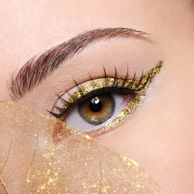 Macro shot of beauty  female eye with golden eyeliner make-up covered artificial yellow  leaf